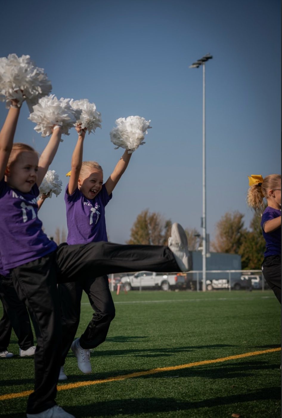 Young cheerleaders performing a high-kick with white poms
