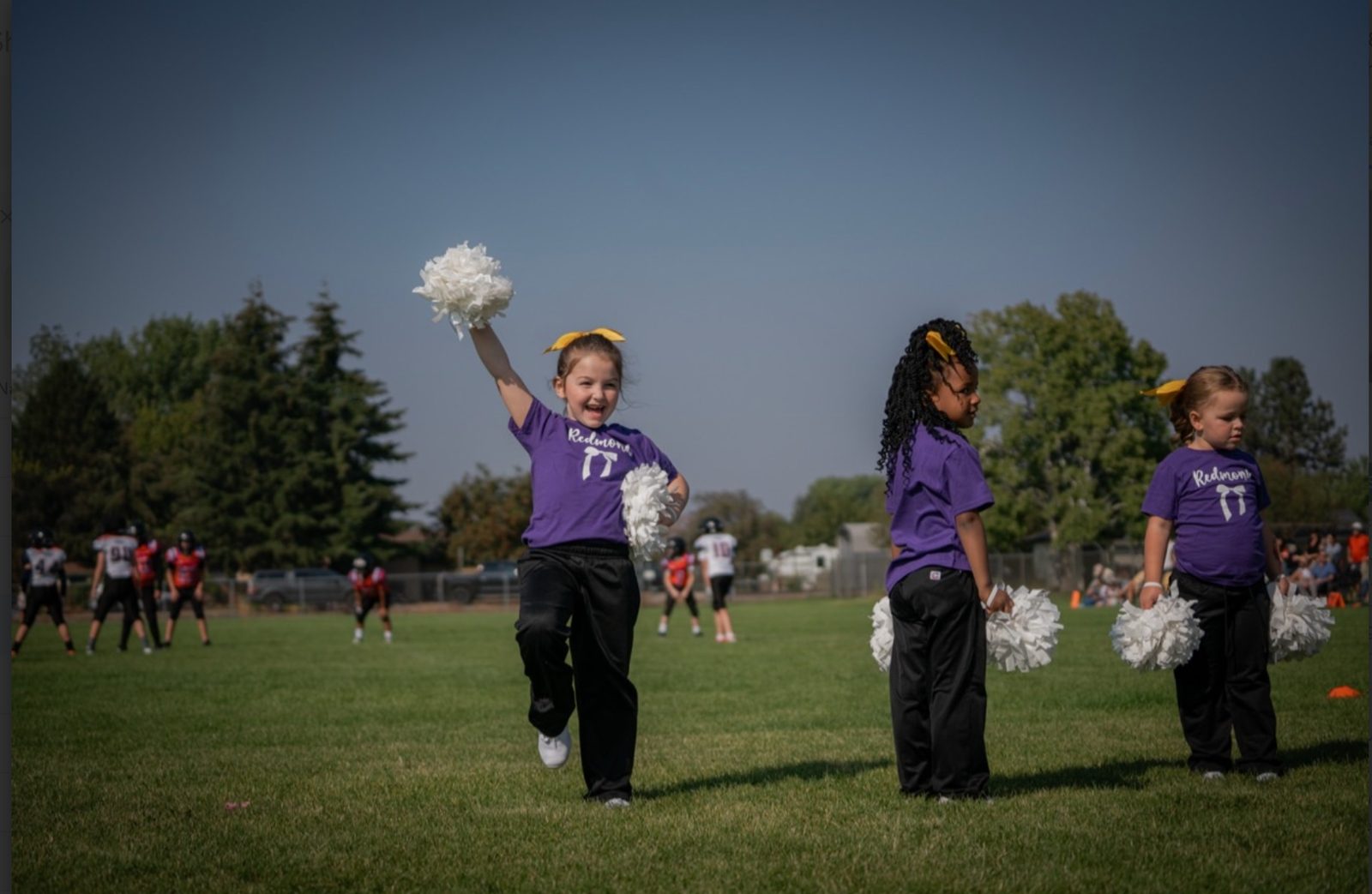Mini cheerleader cheering with a raised pom-pom on the sideline