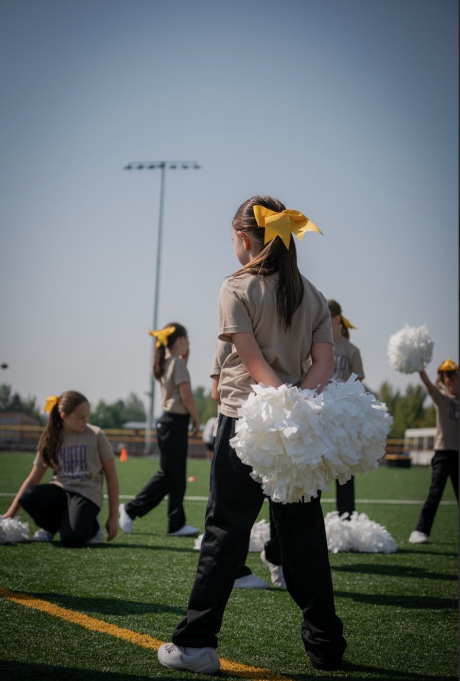 Cheerleader on the field holding white poms behind her back