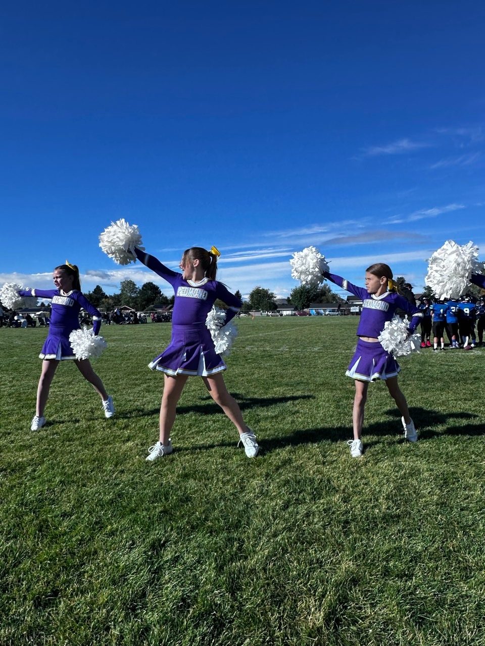 Youth cheerleaders holding a stunt with a flyer lifted on the football field